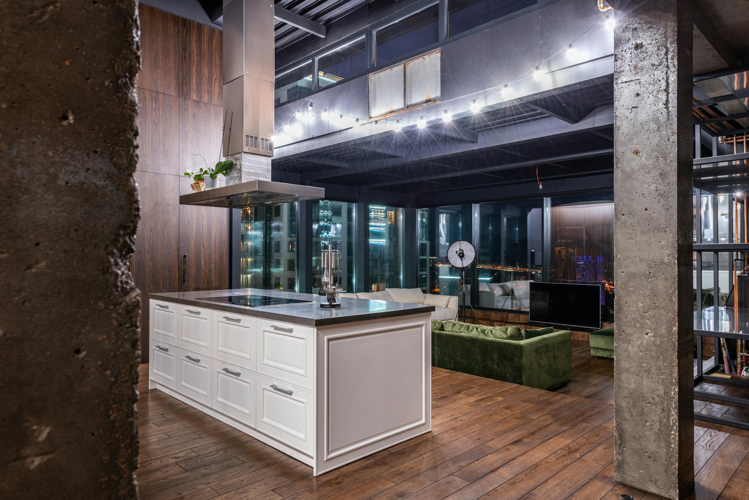 Interior of spacious kitchen area with stylish furniture against living room in modern apartment in evening time